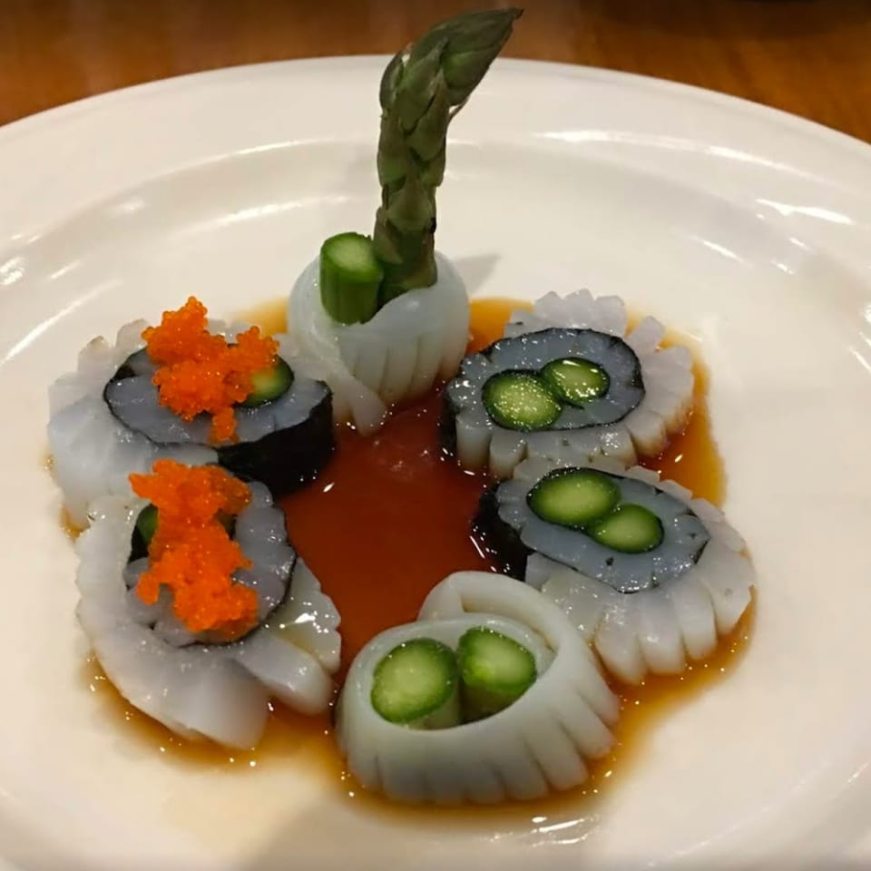 Five pieces of squid sashimi with asparagus and roe, arranged in a circle on a white plate.