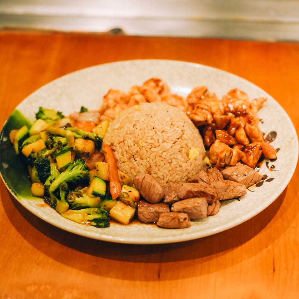 A Japanese hibachi dinner with steak, chicken, shrimp, fried rice, and mixed vegetables on a white plate.