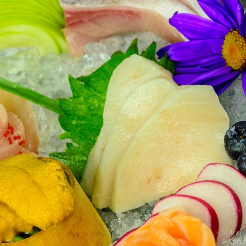 Assorted sashimi and sushi, including uni, on ice with a purple flower garnish.