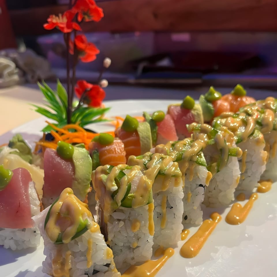 Assorted sushi rolls with salmon, tuna, avocado, and spicy sauce, garnished with red flowers.